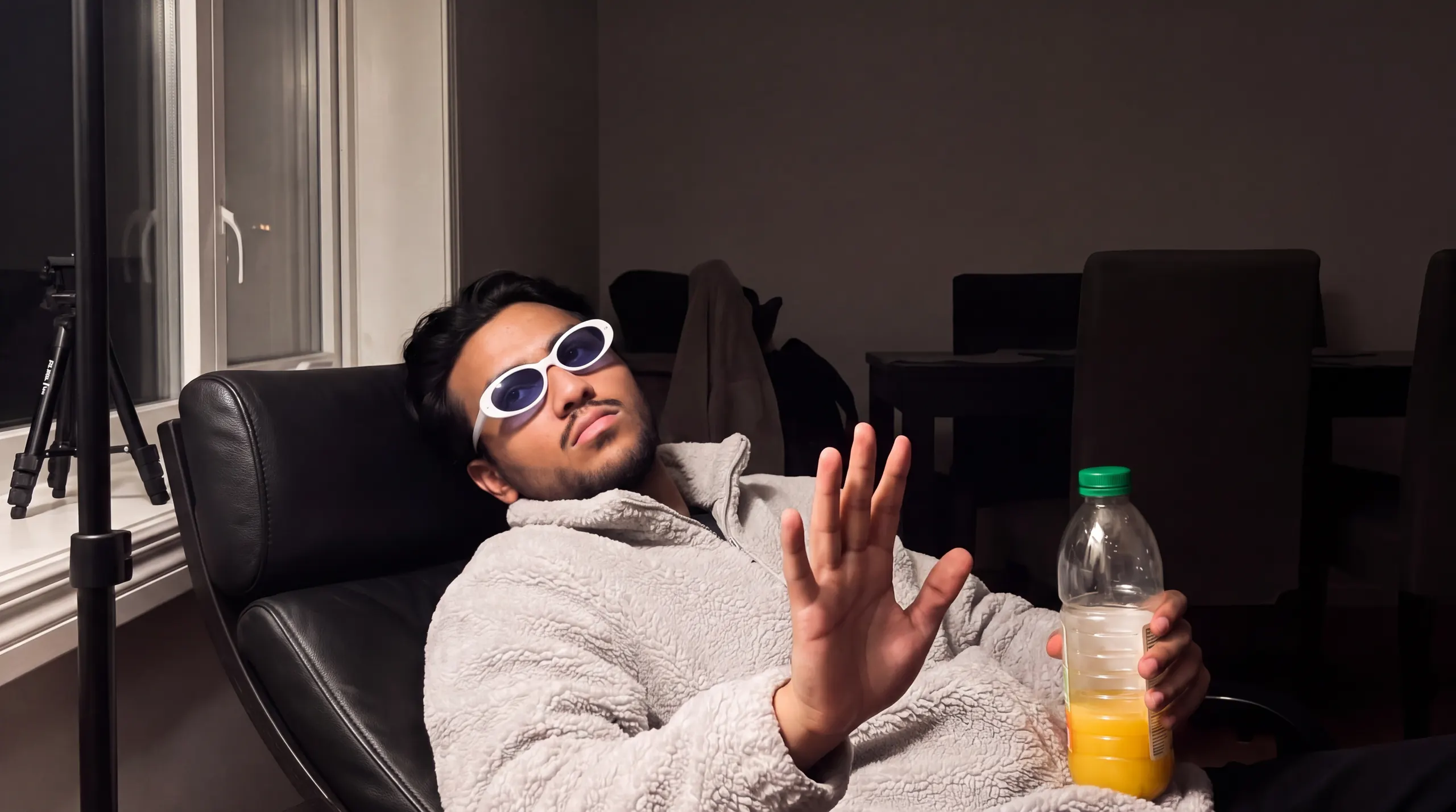 Manu Konar slumped back in a lounge chair in sunglasses, juice bottle in one hand, the other palm-out: chill